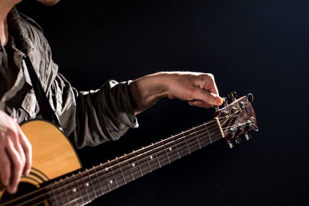 Chitarrista, musica. Un giovane suona una chitarra acustica su uno sfondo nero isolato. Luce puntata