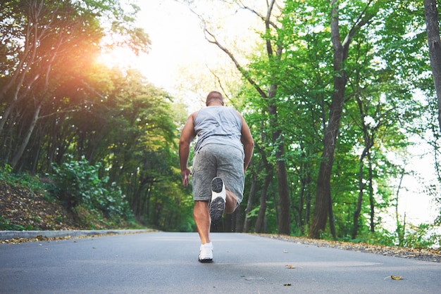 Chiuda in su dei piedi dell'uomo giovane corridore che corre lungo la strada nel parco.