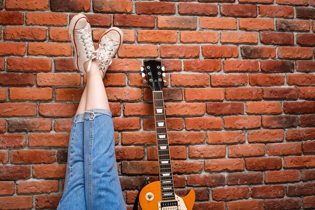 Chiuda in su dei piedini e della chitarra della ragazza sopra la priorità bassa del mattone.