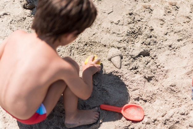 Chiuda in su del bambino che gioca con la sabbia in spiaggia