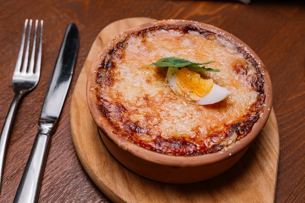 Chiuda in su del piatto italiano arrostito in vaschetta delle terraglie guarnita con formaggio fuso e la metà dell'uovo sodo