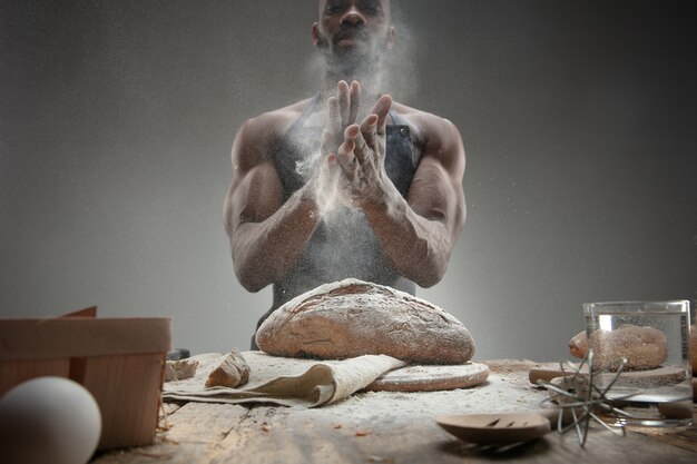 Chiuda in su dell'uomo afro-americano cuochi cereali freschi, pane, crusca sulla tavola di legno. Mangiare gustoso, nutrizione, prodotto artigianale. Cibo senza glutine, stile di vita sano, produzione biologica e sicura. Fatto a mano.