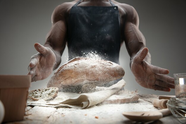 Chiuda in su dell'uomo afro-americano cuochi cereali freschi, pane, crusca sulla tavola di legno. Mangiare gustoso, nutrizione, prodotto artigianale. Cibo senza glutine, stile di vita sano, produzione biologica e sicura. Fatto a mano.