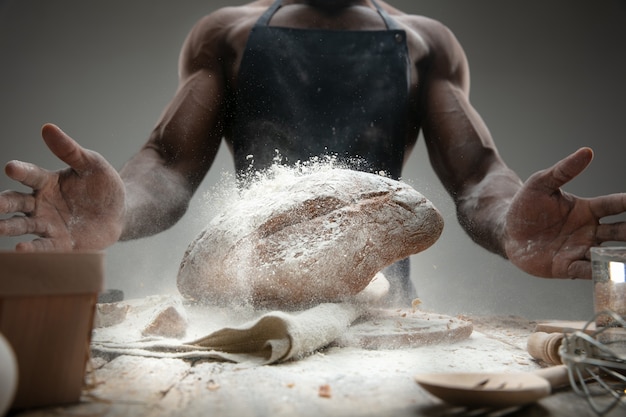 Chiuda in su dell'uomo afro-americano cuochi cereali freschi, pane, crusca sulla tavola di legno. Mangiare gustoso, nutrizione, prodotto artigianale