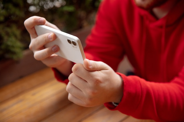 Chiuda in su dell'uomo che utilizza telefono astuto mobile isolato sul muro bianco. Stile di vita, concetto di moderne tecnologie.