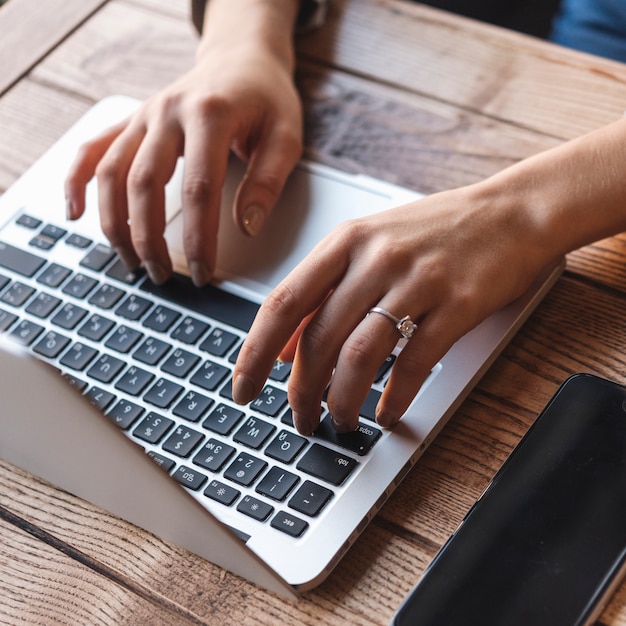 Chiuda in su della donna che digita sul computer portatile nella caffetteria