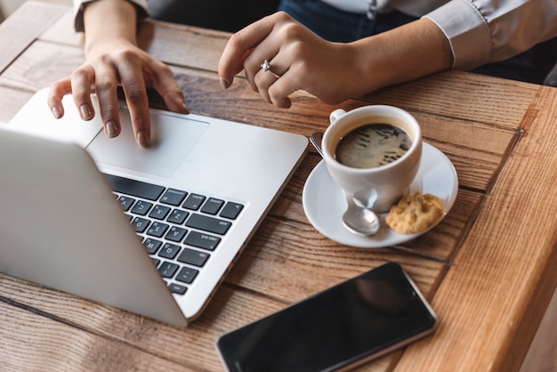 Chiuda in su della donna che digita sul computer portatile nella caffetteria