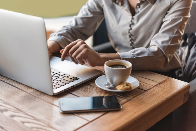 Chiuda in su della donna che digita sul computer portatile nella caffetteria