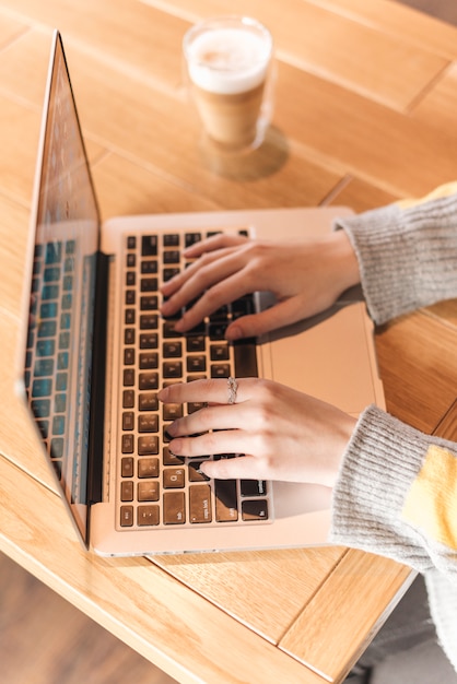 Chiuda in su della donna che digita sul computer portatile nella caffetteria