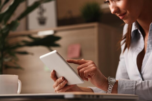 Chiuda in su della donna d'affari sorridente che naviga in Internet sul touchpad al lavoro