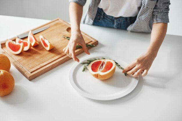 Chiuda in su della ragazza che decora la zolla con la metà del pompelmo e dei rosmarini. Dieta cibo sano.