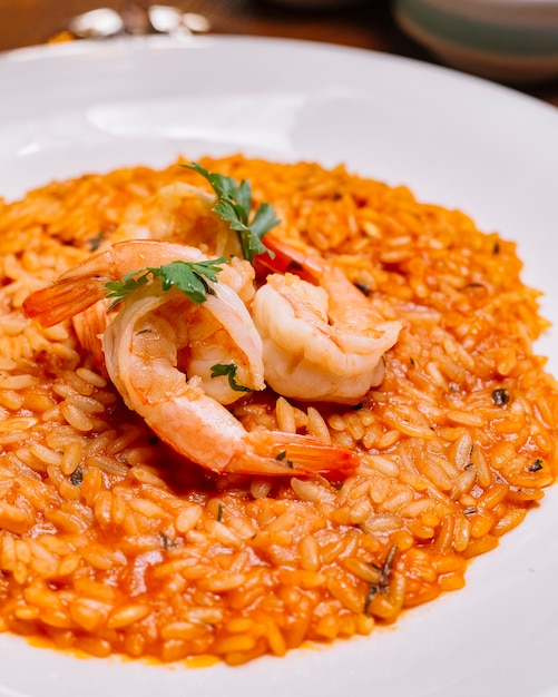 Chiuda in su della zolla del risotto dei frutti di mare con la salsa di pomodori guarnita con gambero