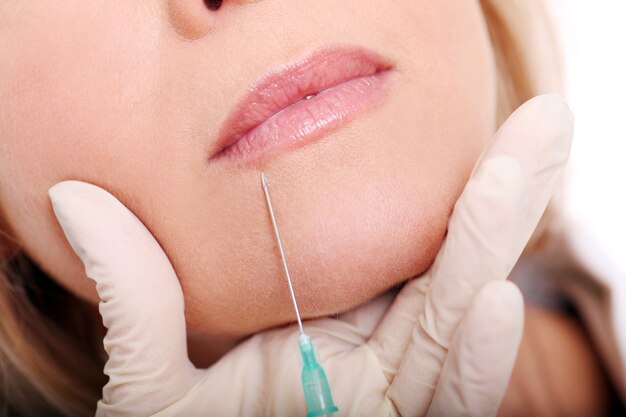 Chiuda in su delle mani del cosmetologo che fa l'iniezione di botox in labbra femminili.