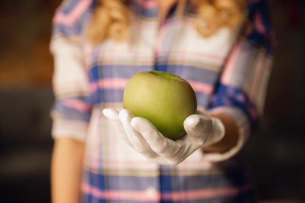 Chiuda in su delle mani femminili in guanti che tengono mela verde, cibo sano, frutta