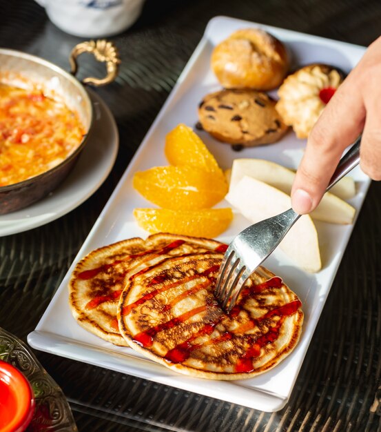 Chiuda su dell'uomo che prende il piccolo pancake con lo sciroppo di fragole