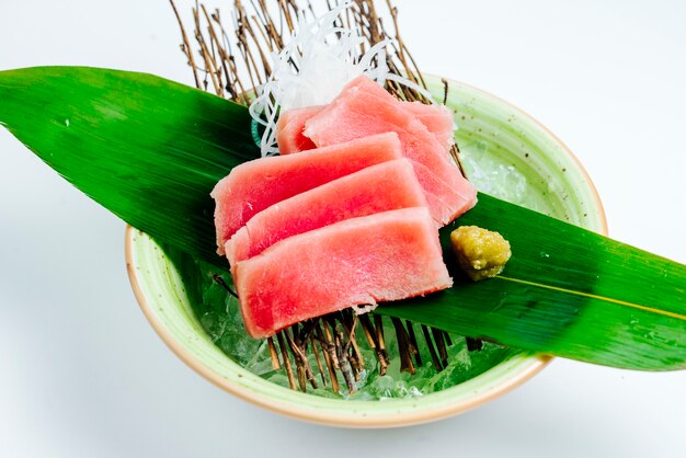 Chiuda su della ciotola del sashimi di tonno servita sul bordo del bastone nel fondo bianco