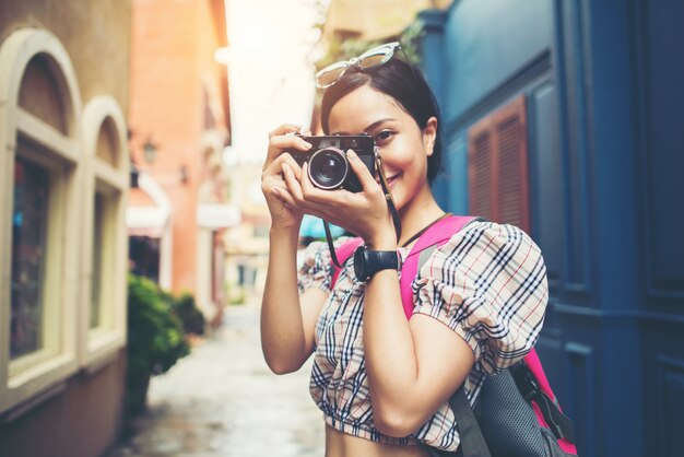 Chiuda su dello zaino della donna dei giovani pantaloni a vita bassa che intraprende la presa della foto con la sua macchina fotografica in urbano.