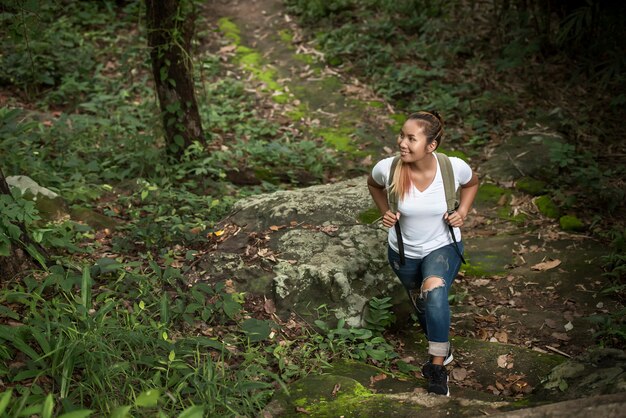 Chiuda su di giovane viaggiatore con zaino e sacco a pelo che cammina attraverso la foresta soddisfatta della natura. Concetto di viaggio