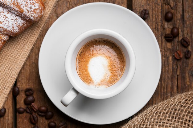 Chiuda sul caffè espresso con i semi del caffè e del croissant