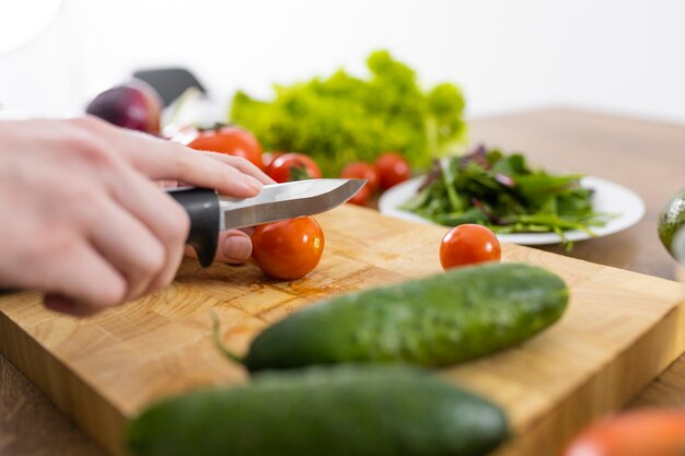 Chiuda sul pomodoro di taglio della mano con il coltello