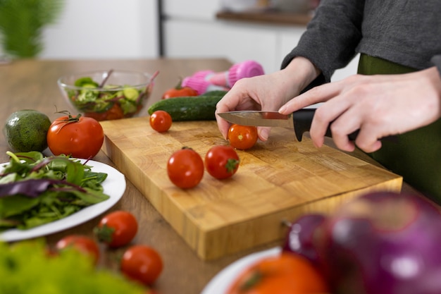 Chiuda sul pomodoro di taglio della mano sulla tavola di legno