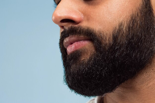 Chiuda sul ritratto del volto di giovane uomo indù con barba e labbra sullo spazio blu