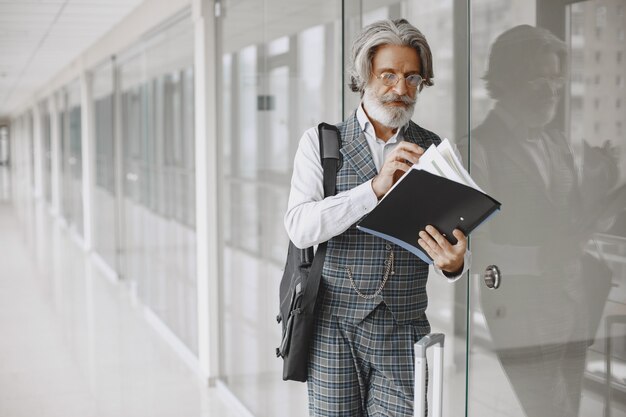 Chiuda sul ritratto dell'uomo antiquato ghignante. Uomo elegante in ufficio. Anziano con documenti.