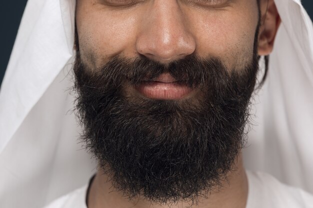 Chiuda sul ritratto dell'uomo d'affari arabo saudita. Volto di giovane modello maschile con la barba, sorridente. Concetto di affari, finanza, espressione facciale, emozioni umane.