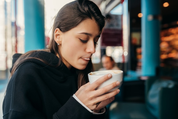 Chiuda sul ritratto della donna graziosa che beve caffè. Signora che tiene una tazza bianca con la mano.