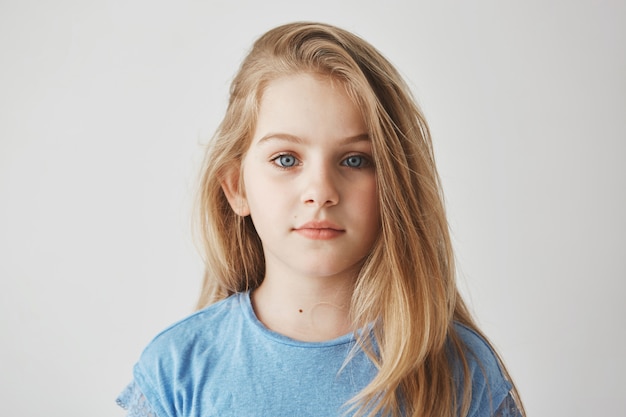 Chiuda sul ritratto di bella bambina con capelli lunghi chiari e grandi occhi azzurri con espressione rilassata.