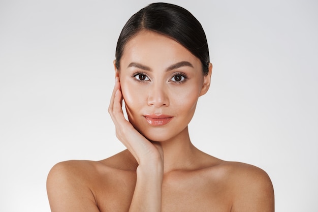 Chiuda sul ritratto di bella donna con trucco naturale che posa alla macchina fotografica con il contatto del suo fronte, isolato sopra bianco