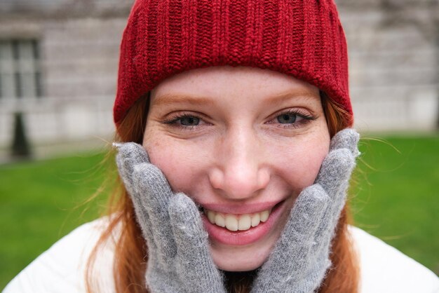 Chiuda sul ritratto di bella donna rossa in guanti caldi del cappello lavorato a maglia rosso che sorride e che sembra felice