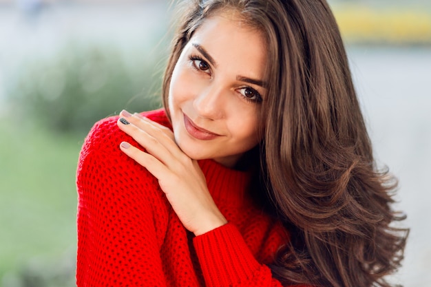 Chiuda sul ritratto di bellezza della donna castana con i capelli lunghi ondulati, sorriso sveglio che si rilassa nel parco di autunno.