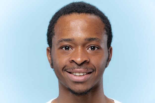 Chiuda sul ritratto di giovane uomo afro-americano in camicia bianca sullo spazio blu