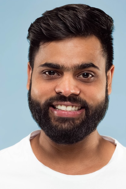 Chiuda sul ritratto di giovane uomo indiano con la barba in camicia bianca isolata. In piedi e sorridente.