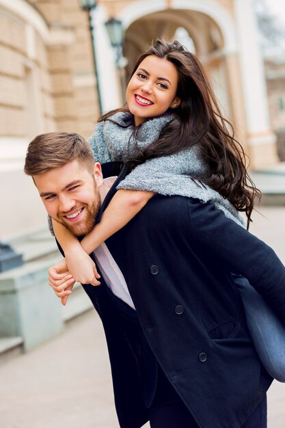 Chiuda sul ritratto di moda di giovane ragazza alla moda glamour e ragazzo innamorato. Coppia camminare per strada in autunno soleggiato. Caldi colori autunnali. Indossa un vestito nero alla moda.