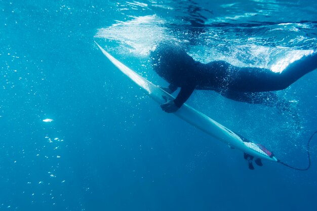 Chiuda sull'uomo con la tavola da surf sott'acqua