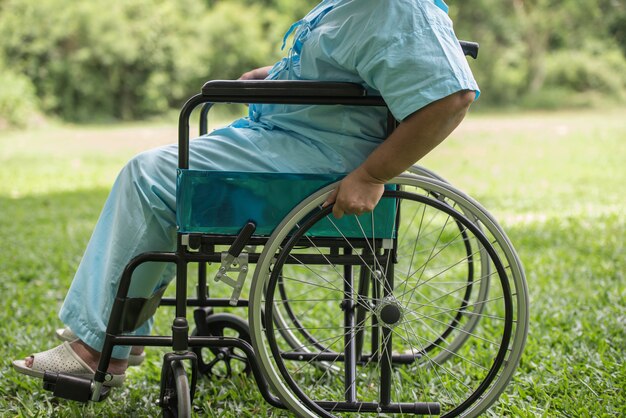 Chiuda sulla donna anziana sola che si siede sulla sedia a rotelle al giardino in ospedale