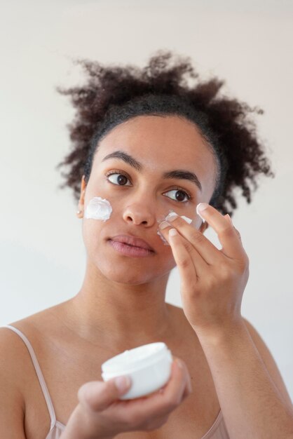 Chiuda sulla donna che usando crema per il viso