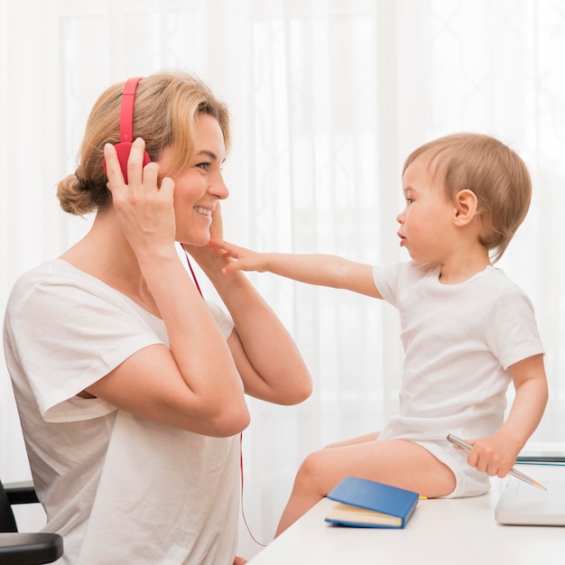 Chiuda sulla madre con le cuffie e il bambino sullo scrittorio