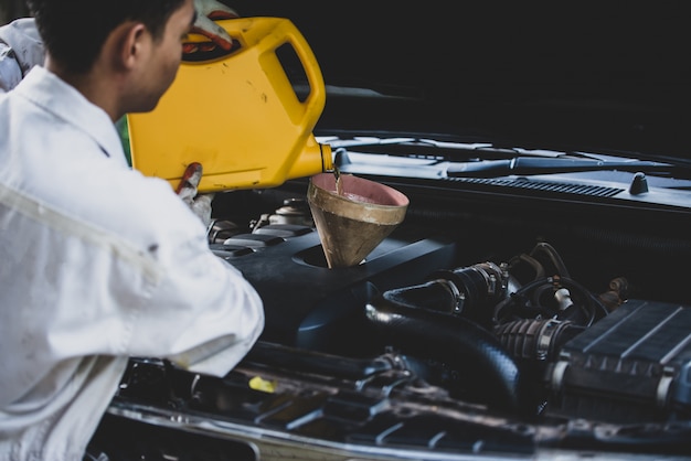 Chiuda sulla mano del meccanico automatico che versa e che sostituisce l'olio fresco nel motore di automobile al garage di riparazione automatica. Manutenzione dell'automobile e concetto di industria