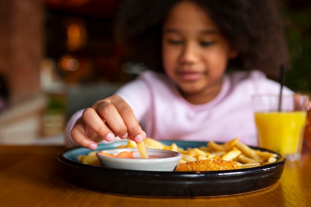 Chiuda sulla ragazza sfocata che mangia patatine fritte