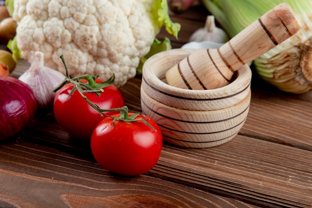 Chiuda sulla vista dei pomodori e di altre verdure con il frantoio di aglio su fondo di legno