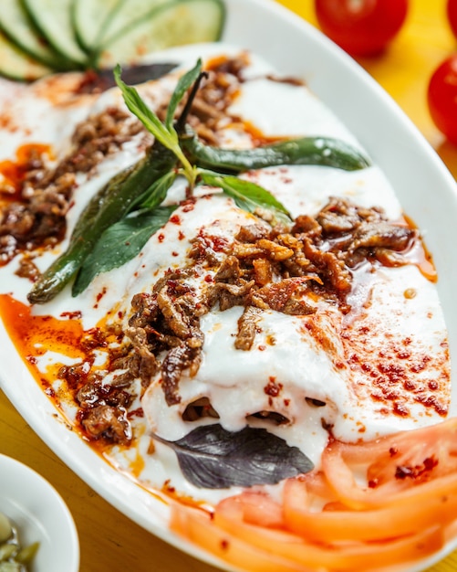 Chiuda sulla vista del kebab turco dell'iskender servito con yogurt acido sul piatto bianco