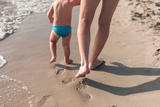 Chiuda sulla vista del padre e del figlio che camminano sulla spiaggia