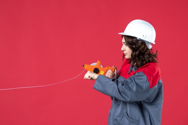 Chiuda sulla vista dell'architetto femminile occupato in uniforme con nastro di misurazione di apertura del cappello duro sulla parete rossa