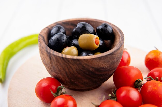 Chiuda sulla vista della ciotola di oliva e di pomodori sul tagliere