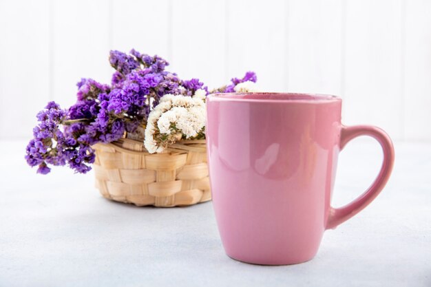 Chiuda sulla vista della tazza di tè con i fiori su superficie bianca