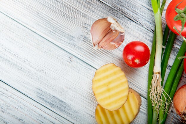 Chiuda sulla vista delle verdure come pomodoro e scalogno della patata affettati aglio dalla destra e fondo di legno con lo spazio della copia