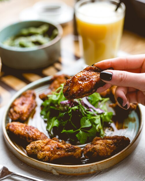 Chiuda sulla vista di una mano femminile che tiene l'ala di pollo fritto